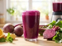 Copo de suco de beterraba para a circulação feito na hora, cercado por beterrabas cruas, laranja, gengibre e hortelã sobre bancada de madeira